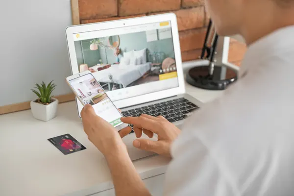 Man with mobile phone booking room in hotel online at home